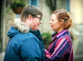 Leon Harrop as Ralph and Sarah Gordy as Katie in Ralph & Katie, stood outside the bakery looking into each other’s eyes. He’s wearing a thick blue coat and she is wearing a red and purple striped shirt (Credit: BBC/ITV Studios/Ben Blackall)