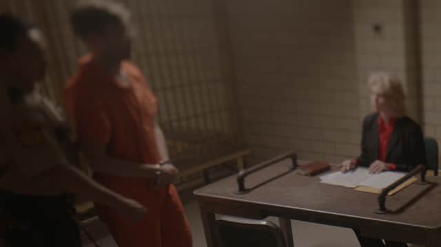 A blurry image of a man in a prison jumpsuit, being lead to a sitdown interview (Credit: Netflix)