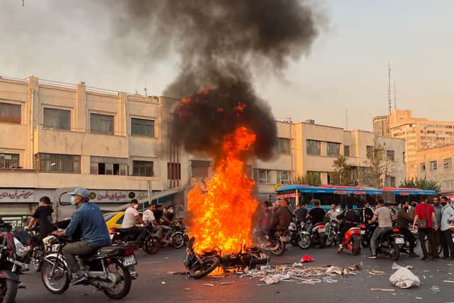 TOPSHOT - A picture obtained by AFP outside Iran, shows people gathering next to a burning motorcycle in the capital Tehran on October 8, 2022. - Iran has been torn by the biggest wave of social unrest in almost three years, which has seen protesters, including university students and even young schoolgirls chant "Woman, Life, Freedom". (Photo by AFP) (Photo by -/AFP via Getty Images)