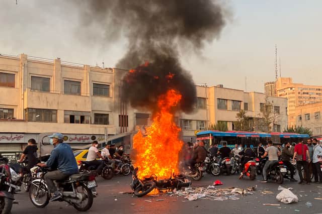 TOPSHOT - A picture obtained by AFP outside Iran, shows people gathering next to a burning motorcycle in the capital Tehran on October 8, 2022. - Iran has been torn by the biggest wave of social unrest in almost three years, which has seen protesters, including university students and even young schoolgirls chant "Woman, Life, Freedom". (Photo by AFP) (Photo by -/AFP via Getty Images)
