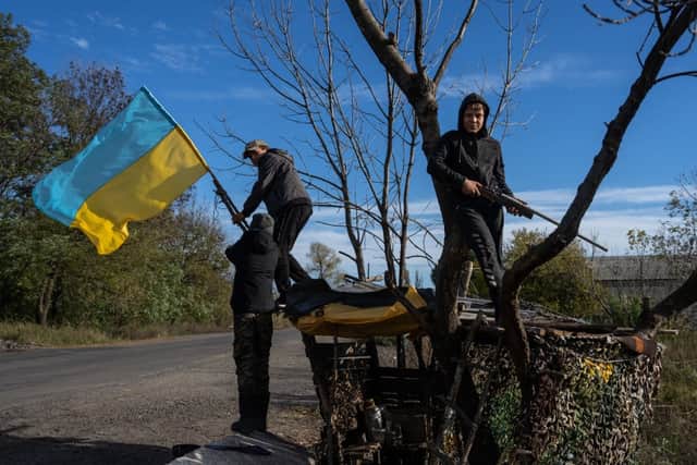 A boy holds a toy rifle as his friends adjust a Ukrainian flag hanging from a tree by the roadside in Dubove, Kharkiv oblast, Ukraine (Photo: Carl Court/Getty Images)
