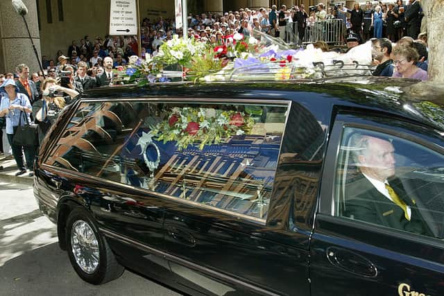 Thousands of people gather as the hearse carrying the coffin of Australian country music icon Slim Dusty leaves St Andrew’s Anglican church in central Sydney after a state funeral, 26 September 2003 (Photo: WILLIAM WEST/AFP via Getty Images)