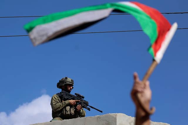 A man waves a Palestinian flag while an Israeli solder looks on during clashes in the village of Deir Sharaf near the western entrance of the city of Nablus in the occupied West Bank. Credit: JAAFAR ASHTIYEH/AFP via Getty Images