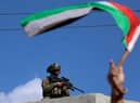 A man waves a Palestinian flag while an Israeli solder looks on during clashes in the village of Deir Sharaf near the western entrance of the city of Nablus in the occupied West Bank. Credit: JAAFAR ASHTIYEH/AFP via Getty Images
