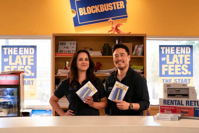 Melissa Fumero as Eliza and Randall Park as Timmy in Blockbuster, holding video tape and smiling (Credit: Ricardo Hubbs/Netflix)