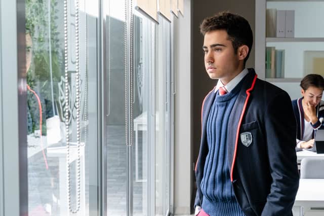 Ander Puig as Nico in Elite, wearing a blue school uniform blazer and looking out the window (Credit: Netflix)