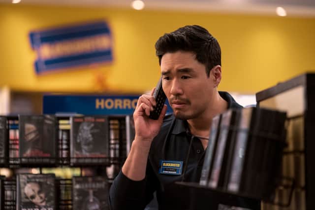 Randall Park as Timmy in Blockbuster, answering the phone next to a shelf of Horror DVDs (Credit: Ricardo Hubbs/Netflix)