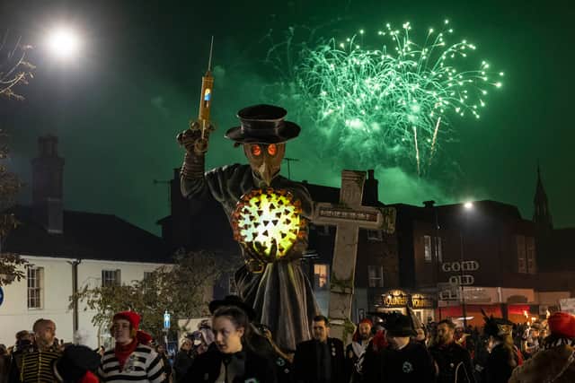 LEWES, ENGLAND - NOVEMBER 05: People walk in front of an effigy holding a hypodermic needle, a Covid-19 virus cell and a tombstone as they take part in the parade at the annual Lewes Bonfire Night Celebrations on November 5, 2021 in Lewes, England. The event commemorates the memory of the seventeen Protestant martyrs as Bonfire Societies parade through the narrow streets. The evening comes to an end with the burning of effigies, or 'guys' usually representing Guy Fawkes, who died in 1605 after an unsuccessful attempt to blow up The Houses of Parliament, and other topical figures. The annual parade was cancelled last year due to the Covid-19 pandemic. (Photo by Dan Kitwood/Getty Images)