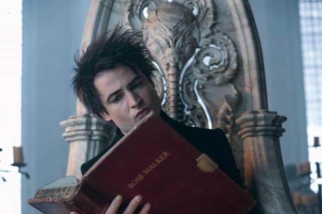 Tom Sturridge as Dream in The Sandman, sat on a faded marble throne, reading a large red-leather bound book with the name ‘Rose Walker’ embossed on the front cover in gold (Credit: Laurence Cendrowicz/Netflix)