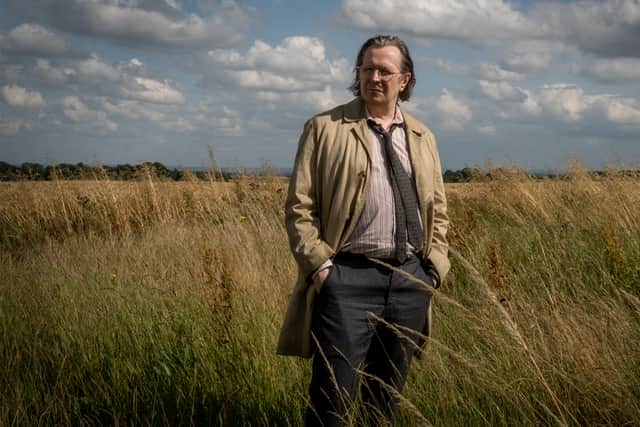 Gary Oldman as Jackson Lamb in Slow Horses S2, stood in a field of wheat, his tan overcoat flapping in the wind (Credit: Apple TV+)