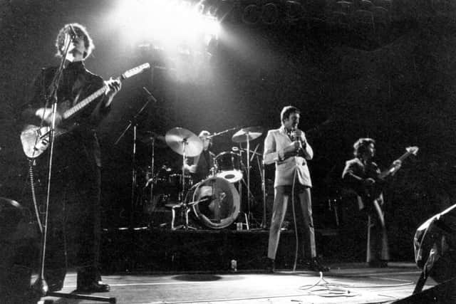 8th December 1976:  Essex-based rhythm and blues band Dr Feelgood performing live at the Hammersmith Odeon, guitarist Wilko Johnson, left, singing, and lead singer Lee Brilleaux standing centre stage.  (Photo by Gary Merrin/Keystone/Getty Images)