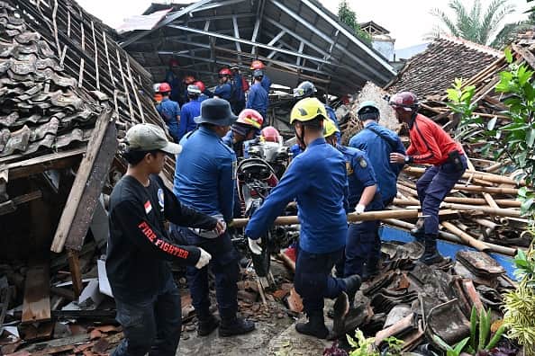 Rescue personnel remove a motorcyle as they work to find a missing child after Indonesia hit by earthquake (AFP via Getty Images)
