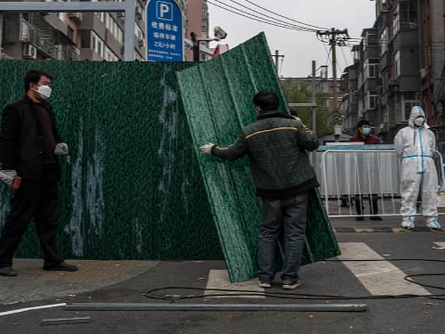 <p>An epidemic control worker wears a protective suit as he watches workers erect a metal barrier fence outside a community under lockdown to prevent the spread of COVID-19 in Beijing, China (Getty Images)</p>