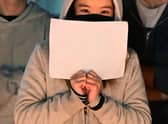 A woman holds a blank sheet of paper as demonstrators protest the deaths caused by an apartment complex fire in Urumqi, Xinjiang, China, at the Langson Library on the campus of the University of California, Irvine, in Irvine, California, on November 29, 2022. - Protests have broken out across China after the Urumqi fire occurred on November 24, 2022. Ten people were reported killed in an apartment building, with delayed fire response due to strict Covid lockdowns being blamed for the deaths. (Photo by Frederic J. BROWN / AFP) (Photo by FREDERIC J. BROWN/AFP via Getty Images)