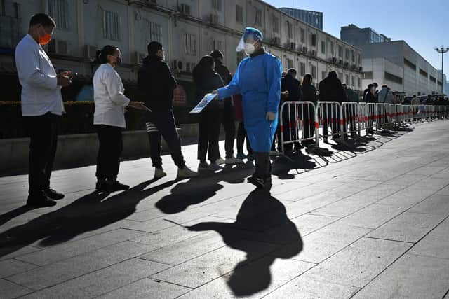 An epidemic control worker has people scan their health codes as they wait in line for a nucleic acid test to detect COVID-19 at a public testing site on November 15, 2022 in Beijing, China.