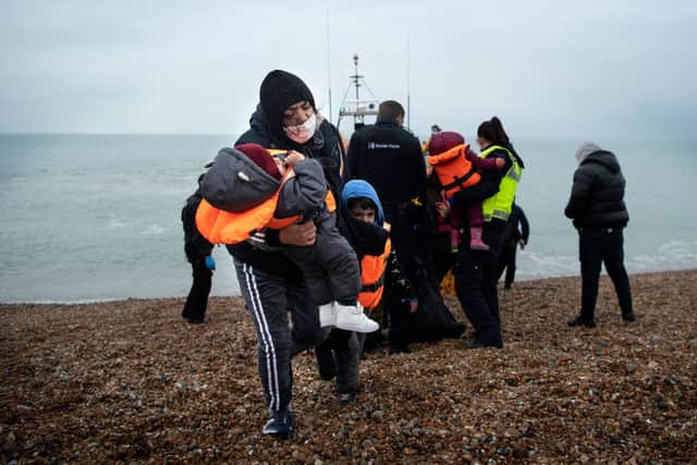 A migrant carries her children after being helped ashore from a RNLI (Royal National Lifeboat Institution) lifeboat at a beach in Dungeness, on the south-east coast of England. Credit: Getty Images
