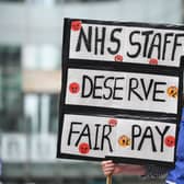 A nurse wearing scrubs holds a placard calling for a pay rise for NHS nursing staff. (Photo by JUSTIN TALLIS/AFP via Getty Images)