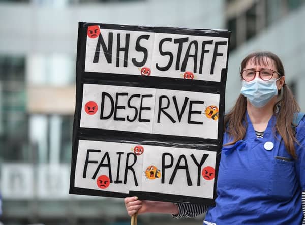 A nurse wearing scrubs holds a placard calling for a pay rise for NHS nursing staff. (Photo by JUSTIN TALLIS/AFP via Getty Images)