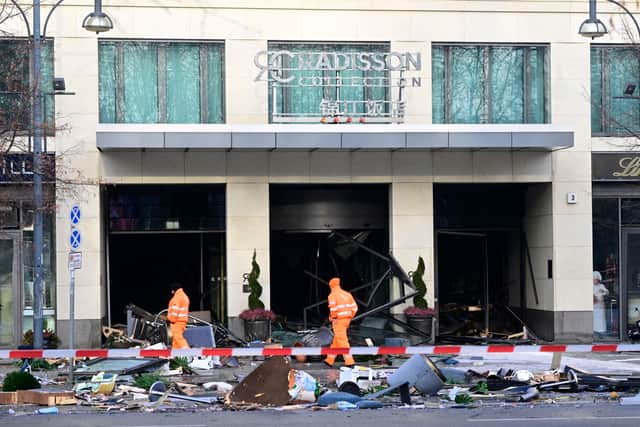 Workers of the city cleaning department walk past debris covering the street in front of the Radisson Blu hotel after a huge aquarium located in the hotel's lobby burst on December 16, 2022 in Berlin. - The 14-metre high AquaDom aquarium has burst and the leaking water has forced the closure of a nearby street, police and firefighters said. Berlin police said on Twitter that as well as causing "incredible maritime damage", the incident left two people suffering injuries from glass shards. The cylindrical aquarium contained over a million litres of water and was home to around 1,500 tropical fish. (Photo by John MACDOUGALL / AFP) (Photo by JOHN MACDOUGALL/AFP via Getty Images)