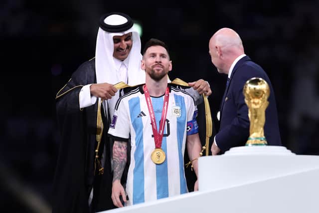 Lionel Messi of Argentina is presented with a traditional robe by Sheikh Tamim bin Hamad Al Thani, Emir of Qatar, while Gianni Infantino, President of FIFA, looks on during the awards ceremony after the FIFA World Cup Qatar 2022 Final match between Argentina and France at Lusail Stadium on December 18, 2022 in Lusail City, Qatar. (Photo by Clive Brunskill/Getty Images)