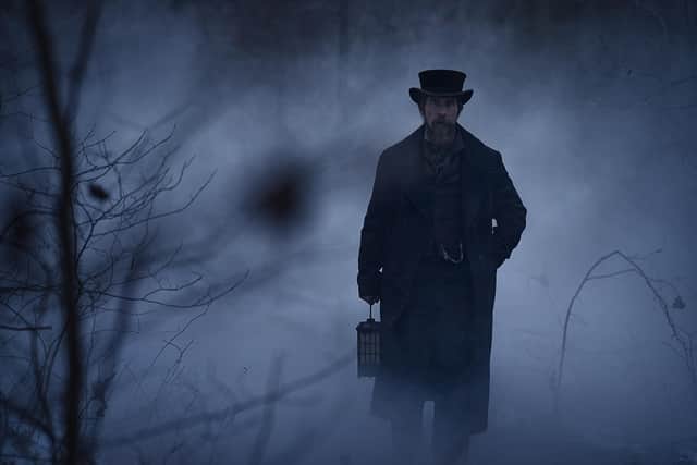 Christian Bale as Augustus Landor in The Pale Blue Eye, emerging from the fog with a lantern (Credit: Scott Garfield/Netflix)