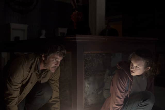 Pedro Pascal as Joel and Bella Ramsay as Ellie in The Last of Us, hiding from an Infected person in the dark (Credit: HBO)