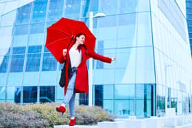 Blue Monday concept. Young executive business woman playing with a red umbrella on a rainy day. She wears a casual urban look, a red coat, jeans and a white blouse. (Itxu - stock.adobe.com)