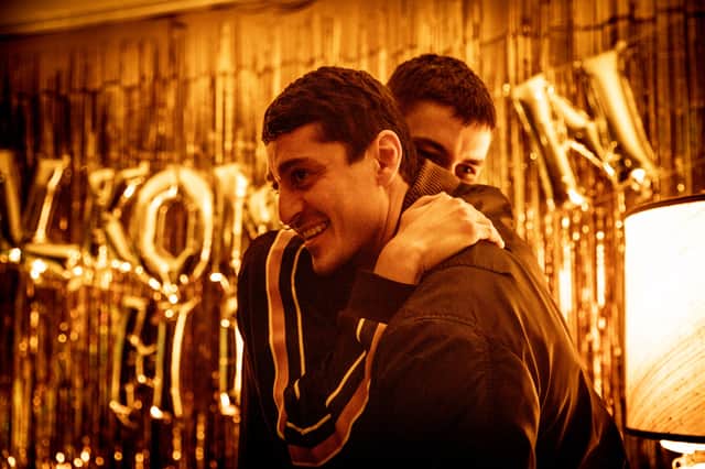 Two men embrace, with golden curtains and balloons behind them, in Top Dog (Credit: Walter Presents)
