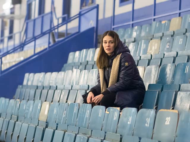 A woman sits in blue stadium seats in The Wall: Cover Your Tracks (Credit: Walter Presents)