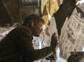 Pedro Pascal as Joel in The Last of Us, looking through a newspaper-covered window (Credit: HBO)