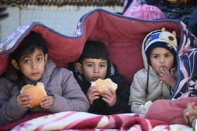 Children eat bread as they sit under a cover in the southeastern Turkish city of Kahramanmaras, two days after a strong earthquake struck the region. (Photo by OZAN KOSE/AFP via Getty Images)