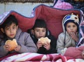 Children eat bread as they sit under a cover in the southeastern Turkish city of Kahramanmaras, two days after a strong earthquake struck the region. (Photo by OZAN KOSE/AFP via Getty Images)