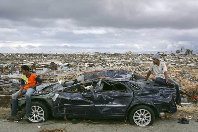 Two tsunami survivors sit on top of a car which was damaged by the tsunami January 9, 2005 in Banda Aceh, Indonesia. An estimated 150,000 were killed in the region after a huge submarine earthquake caused a tsunami wave destroying nearly everything in its path.  (Photo by Dimas Ardian/Getty Images)
