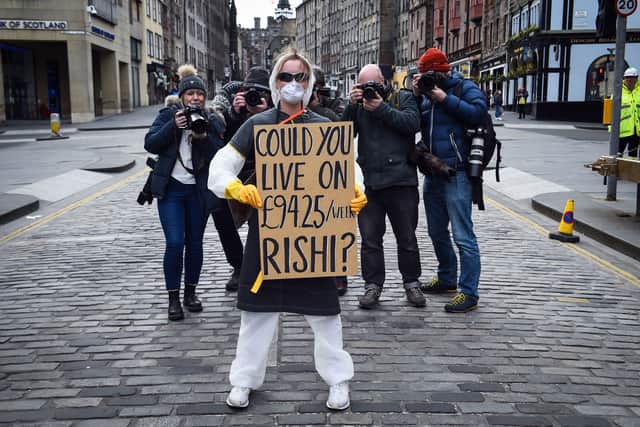 A woman wearing a protective face mask and gloves holds a placard complaining about the lack of support for the self-employed and zero hours contract workers, on the Royal Mile in Edinburgh in Scotland on March 23, 2020