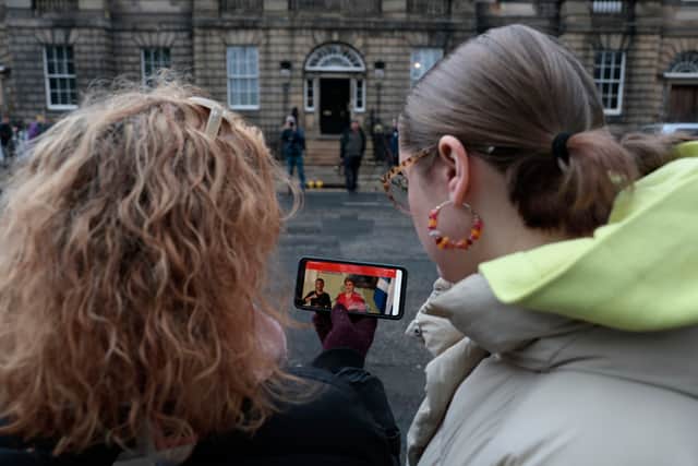 People watch a press conference held by Scotland’s First Minister Nicola Sturgeon on a mobile phone as they gather stand outside of Bute House in Edinburgh (Photo by Jeff J Mitchell/Getty Images)