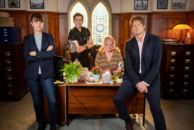 Zahra Ahmadi as DS Esther Williams, Dylan Llewellyn as PC Kelby Hartford, Felicity Montagu as Margo Martins, and Kris Marshall as Humphrey Goodman in Beyond Paradise, positioned around the desk in the Shipton Abbott police station (Credit: Red Planet Pictures/Craig Hardie)