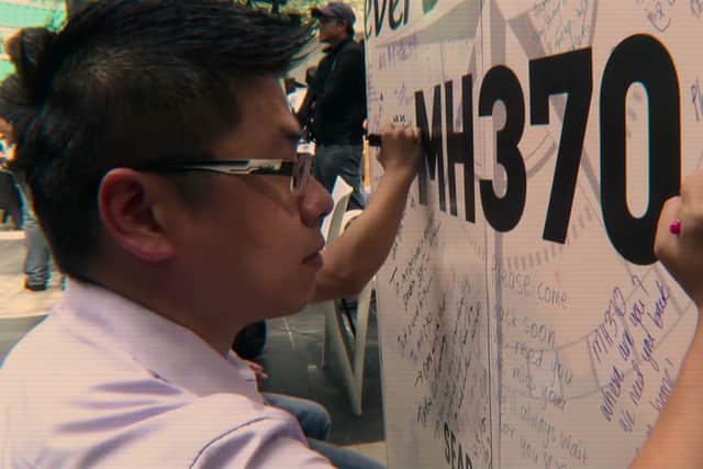 A young man wearing glasses signs his name to a list of tributes to the missing MH370 passengers in a scene from Netflix documentary MH370: The Plane That Disappeared (Credit: Netflix)