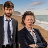 David Tennant as DI Alec Hardy with Olivia Colman as DS Ellie Miller in Broadchurch, the iconic cliff face in the distance behind them (Credit: ITV/Kudos)