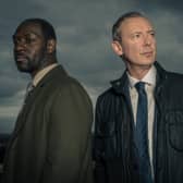Richie Campbell as DS Glenn Branson and John Simm as DI Roy Grace in Grace S3, stormclouds brewing behind them (Credit: ITV)