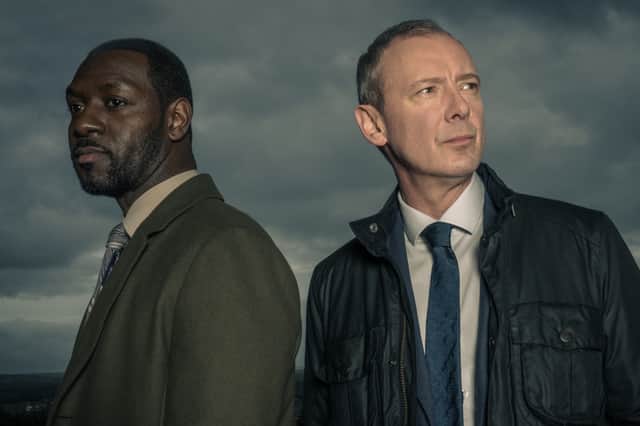 Richie Campbell as DS Glenn Branson and John Simm as DI Roy Grace in Grace S3, stormclouds brewing behind them (Credit: ITV)