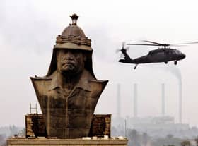 A US military helicopter hovers over a giant bronze bust of Saddam Hussein as workers prepare to dismantle it at the former presidential palace in Baghdad 02 December 2003 (Photo: PETER KUJUNDZIC/AFP via Getty Images)