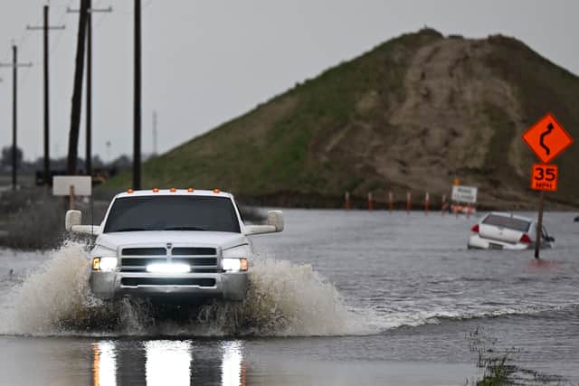 A pickup truck drives on a flooded road out of Alpaugh as a car sits in flooding in the Central Valley during a winter storm in Tulare County near Allensworth, California on 22 March (Photo: PATRICK T. FALLON/AFP via Getty Images)