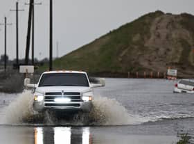 A pickup truck drives on a flooded road out of Alpaugh as a car sits in flooding in the Central Valley during a winter storm in Tulare County near Allensworth, California on 22 March (Photo: PATRICK T. FALLON/AFP via Getty Images)