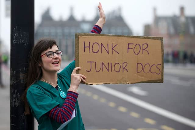 A demonstrator wearing doctor's scrubs holds a placard as she protests during a Junior Doctors' strike outside St Thomas' Hospital in central London on April 6, 2016, against proposed new conditions and pay rates for working unsociable hours. (Photo by JUSTIN TALLIS/AFP via Getty Images)