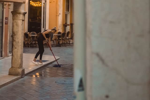 Lady sweeping, Corfu Town, Corfu, 2023, Craig Sinclair. The left-hand framing helps create a sense of motion, of a moment captured unawares. 