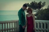 Richard Armitage as William and Charlie Murphy as Anna in Obsession, holding hands on a balcony with the sea behind them (Credit: Netflix)