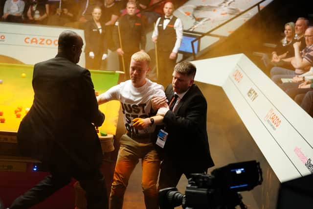 A Just Stop Oil protester is removed after jumping on the table and throwing orange powder during the match between Robert Milkins against Joe Perry during day three of the Cazoo World Snooker Championship at the Crucible Theatre, Sheffield. (Photo: PA/Mike Egerton)