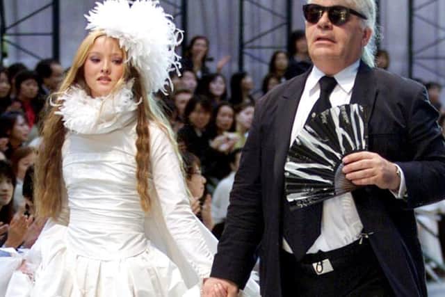 German designer Karl Lagerfeld (R) of Chanel leads Japanese model Devon Aoki wearing a wedding dress during the autumn/winter 2000-2001 Chanel collection in Tokyo 12 May 2000. (ELECTRONIC IMAGE)  AFP PHOTO/Toru YAMANAKA (Photo by TORU YAMANAKA / AFP)        (Photo credit should read TORU YAMANAKA/AFP via Getty Images)