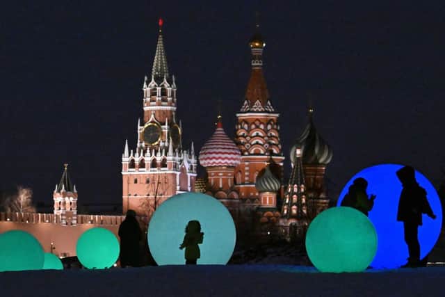 People walk past light installations at Zaryadie park in front of the Spasskaya tower of the Kremlin (L) and the Saint Basil cathedral (R), in  Moscow. (Photo by YURI KADOBNOV/AFP via Getty Images)