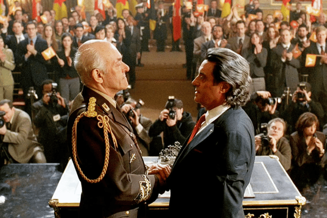 Ian McShane as Silas in Kings, shaking hands with a military leader in front of a crowd of journalists (Credit: NBC)